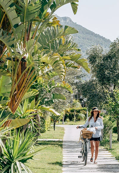 Guest walking a bicycle through the lush tropical garden at D Resort Gocek